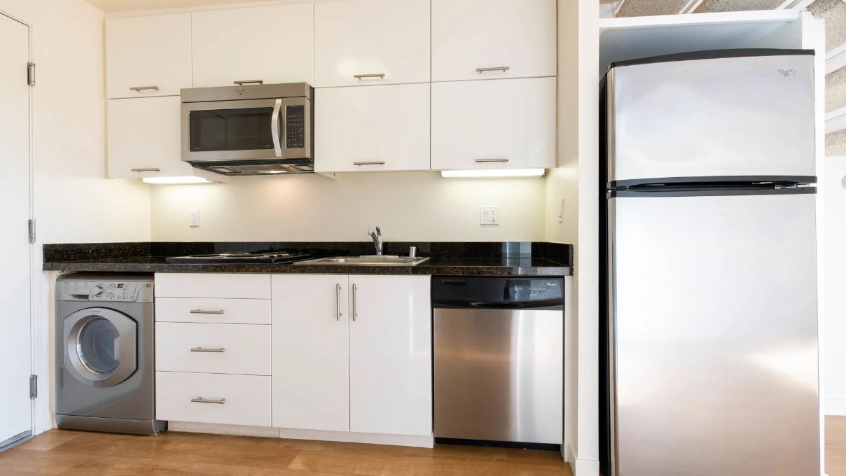 Small, white kitchen with stainless steel appliances; includes washer/dryer, microwave, refrigerator, and sink.