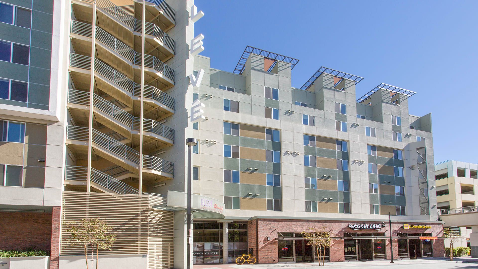 Buildings with balconies and shops at street level under a blue sky.