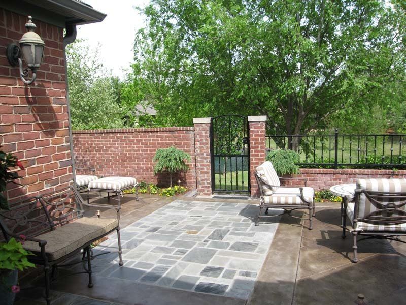 A brick wall surrounds a patio with chairs and a bench
