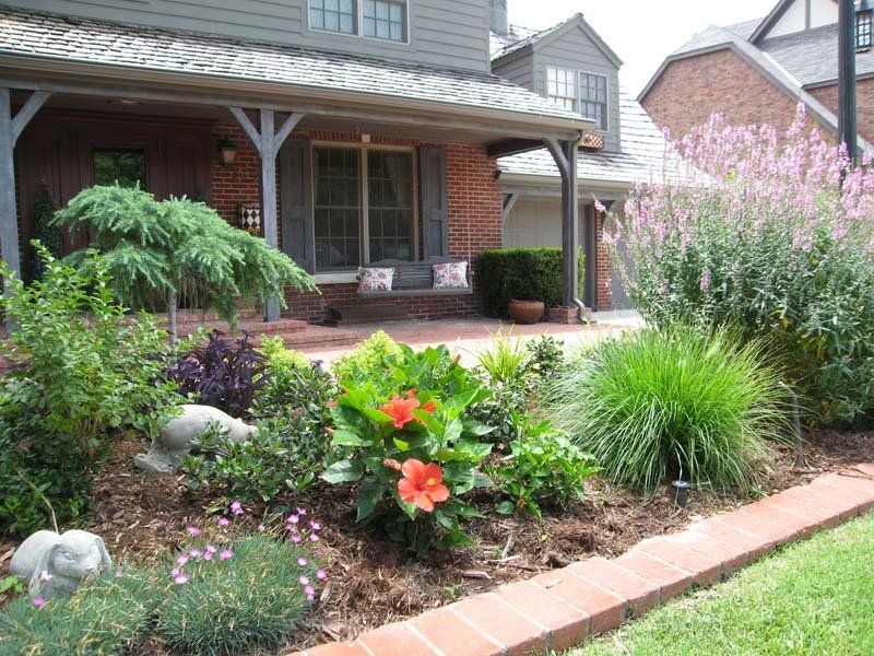 A brick house with a porch and flowers in front of it