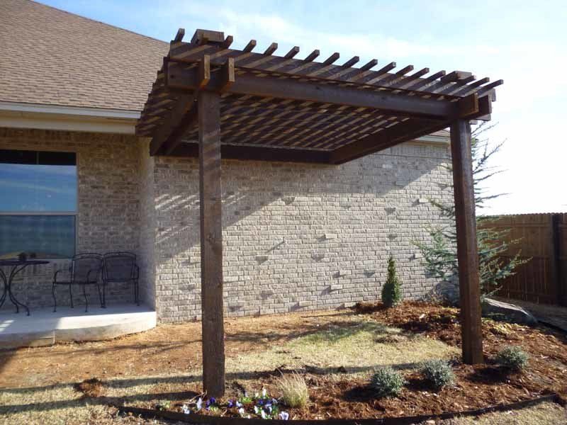 A wooden pergola sits in front of a brick house