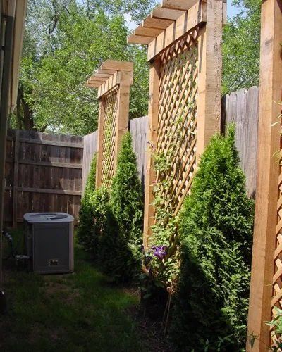 An air conditioner sits in the backyard next to a wooden fence