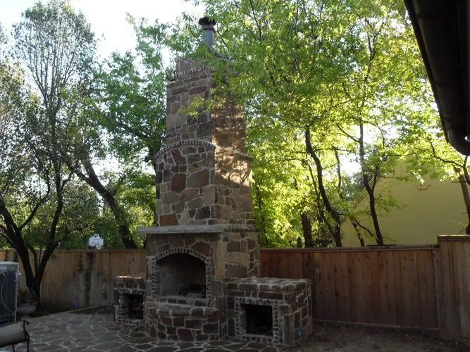 A large stone fireplace is in the backyard of a house.
