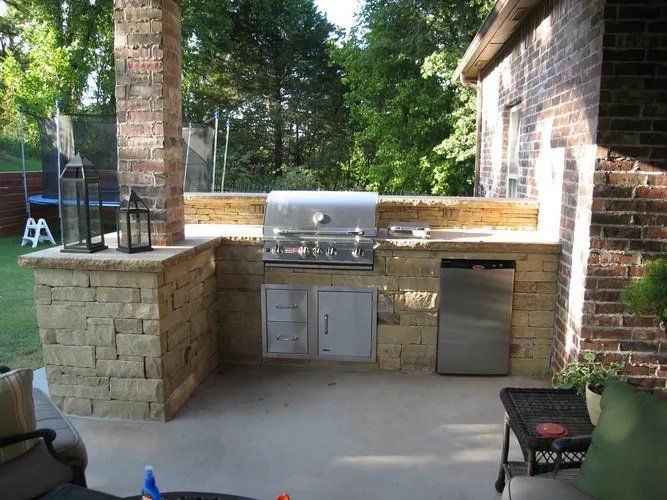 An outdoor kitchen with a grill and a stainless steel refrigerator