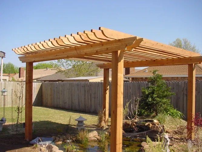 A wooden pergola in a backyard next to a pond