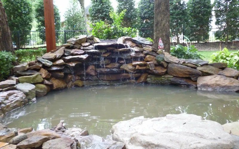 A waterfall is surrounded by rocks and a pond