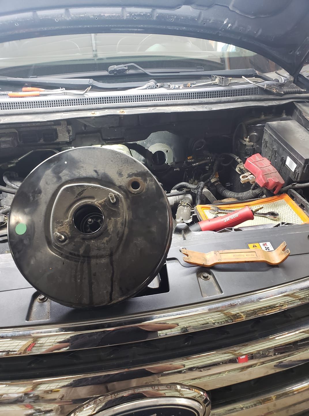 A brake booster is sitting on the hood of a car.