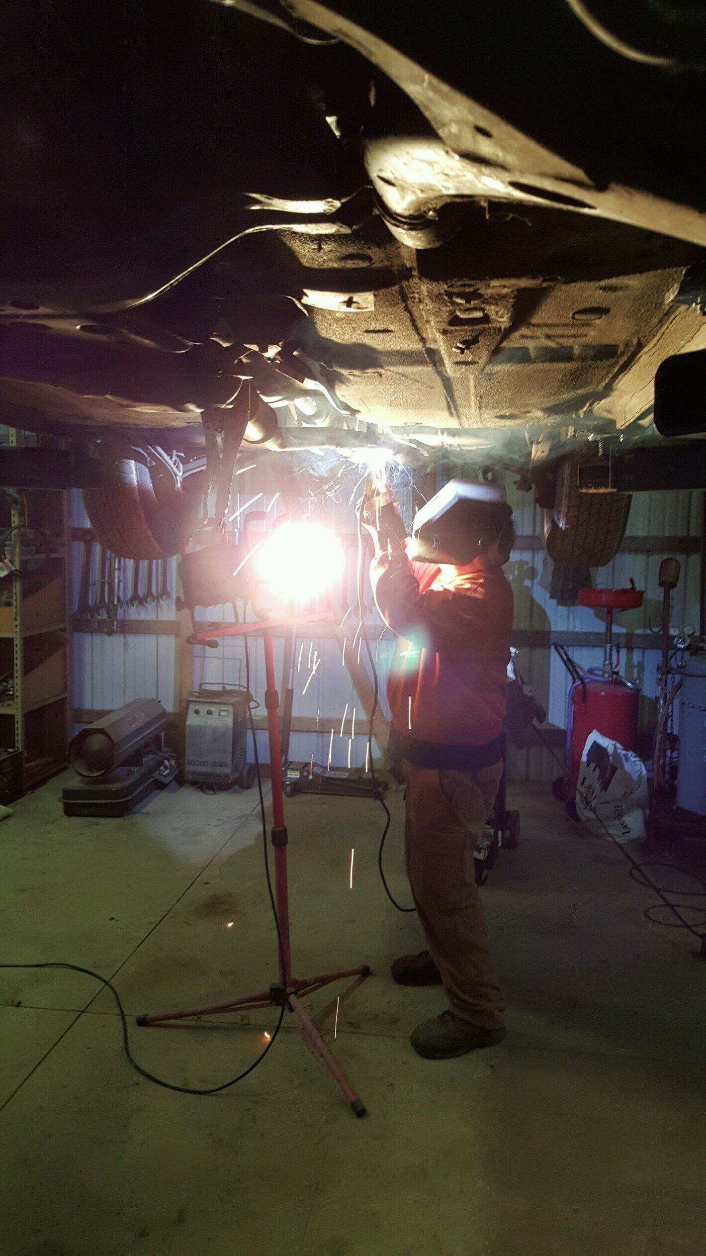 A man is working under a car in a garage with a light.