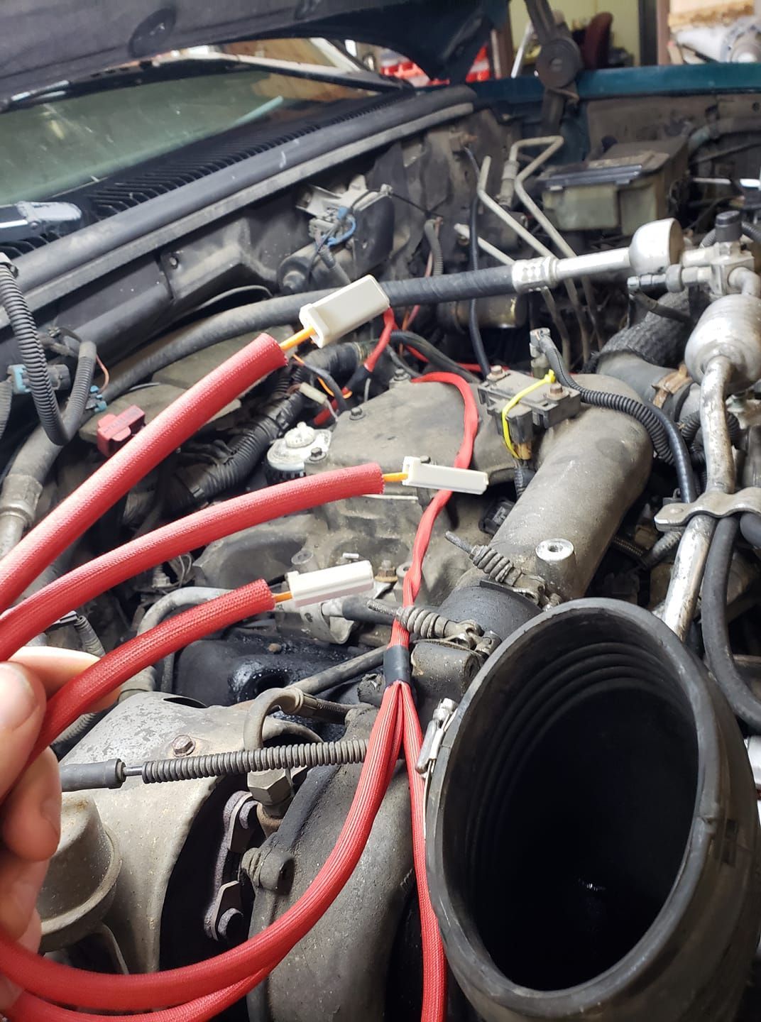 A person is holding a red hose in front of a car engine
