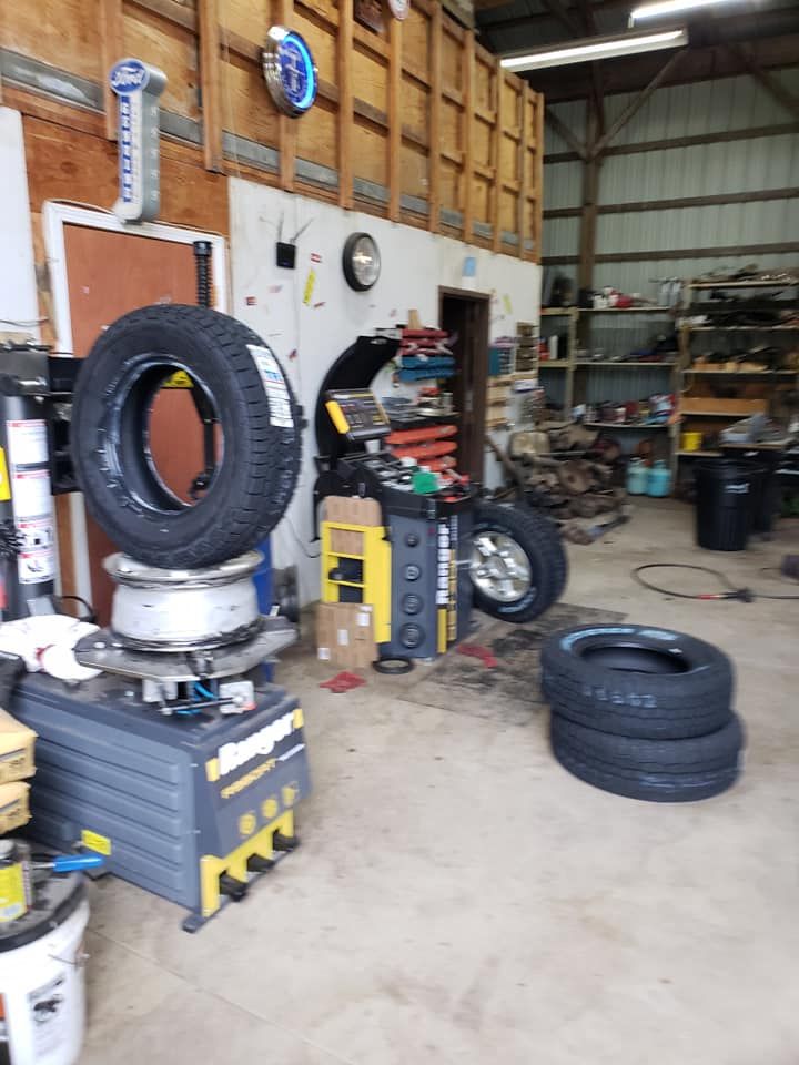 A tire balancing machine is sitting in a garage next to a stack of tires.