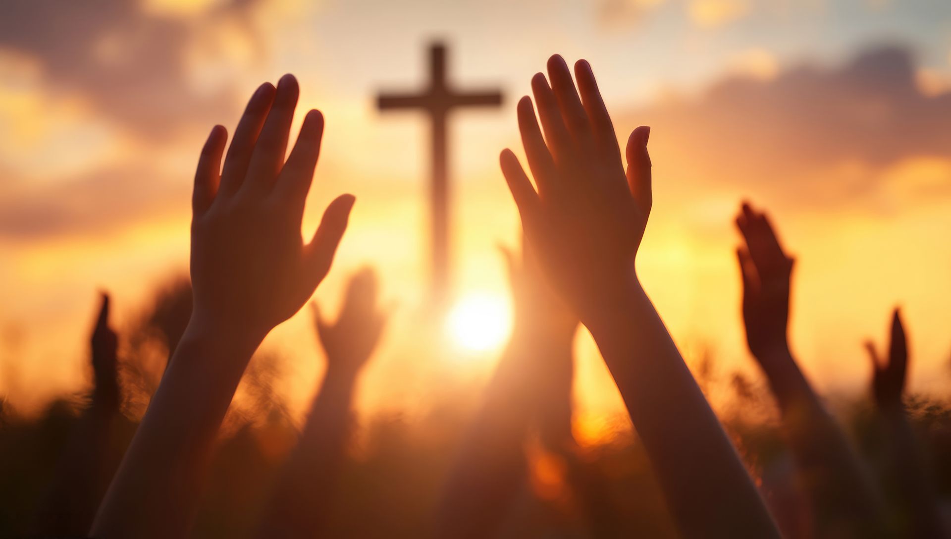 Hands raised in worship towards a cross silhouetted by the sunset, with a warm, golden glow.