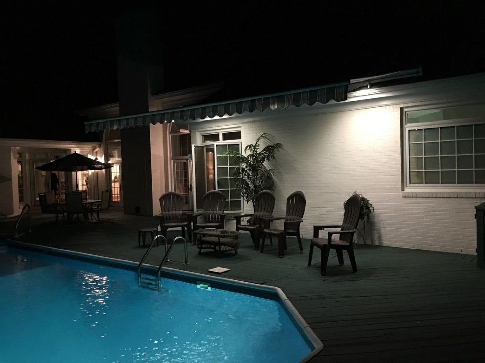 A swimming pool with chairs and tables in front of a house at night.