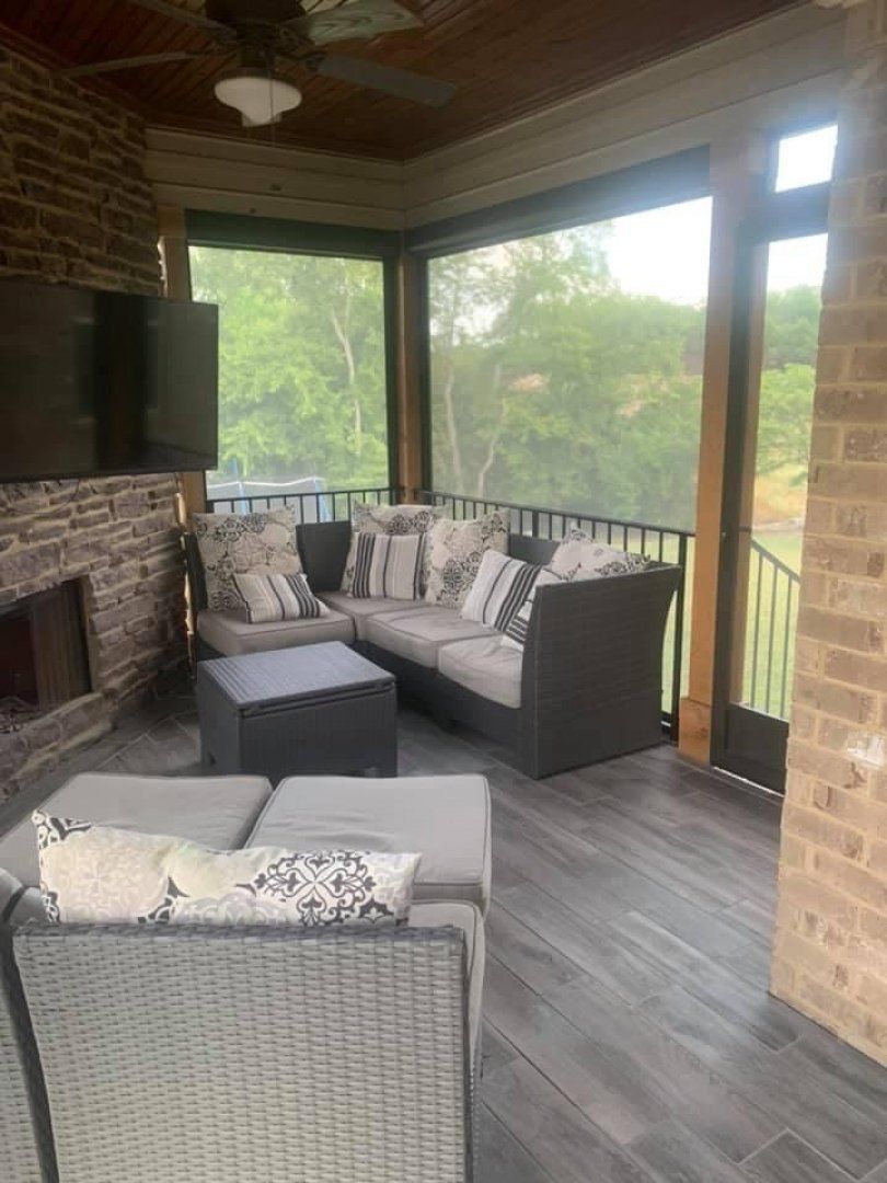 A screened in porch with a couch and chairs and a fireplace.