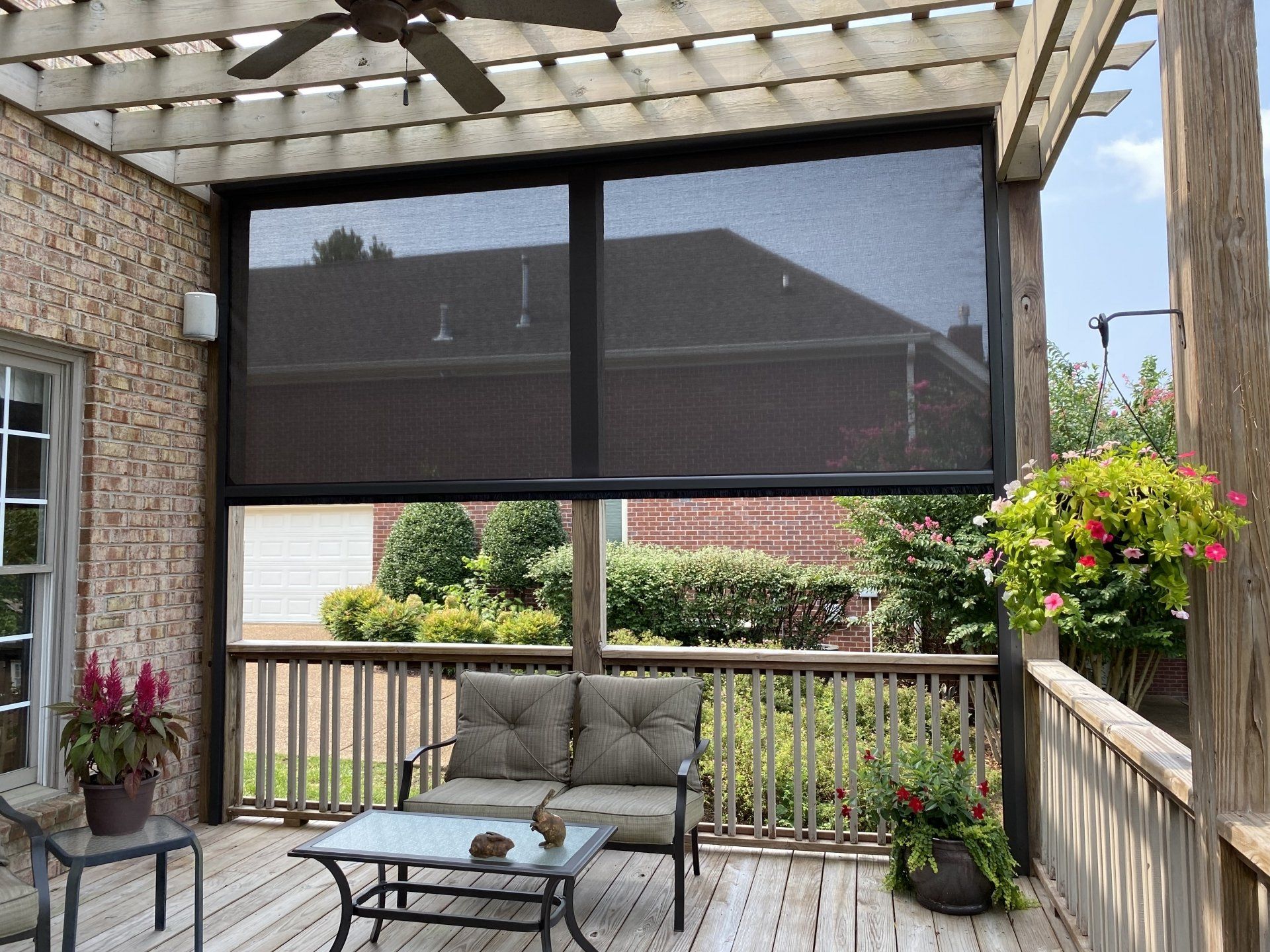A screened in porch with a couch , table , chairs and a ceiling fan.