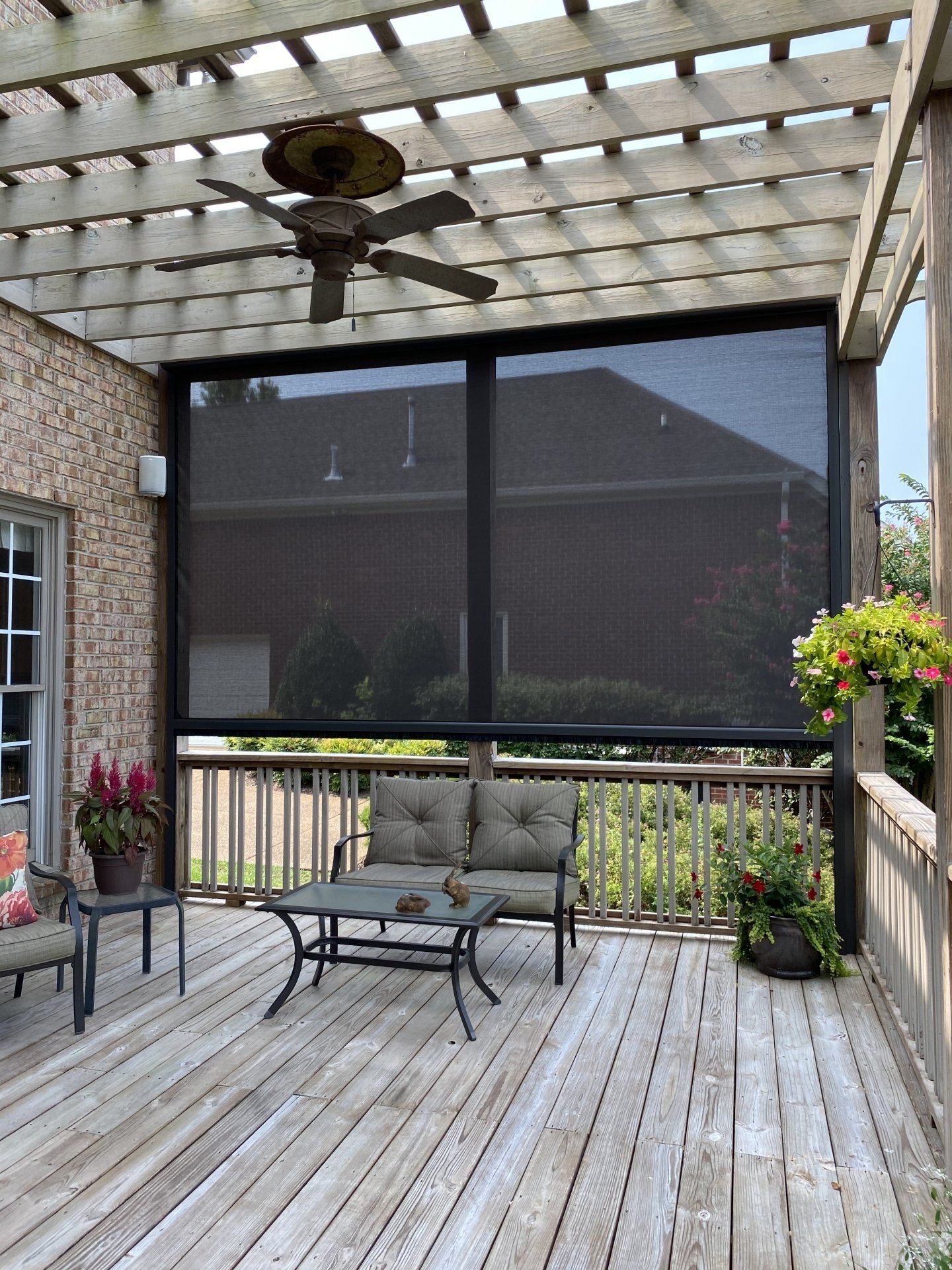 A screened in porch with a couch , table , chairs and a ceiling fan.