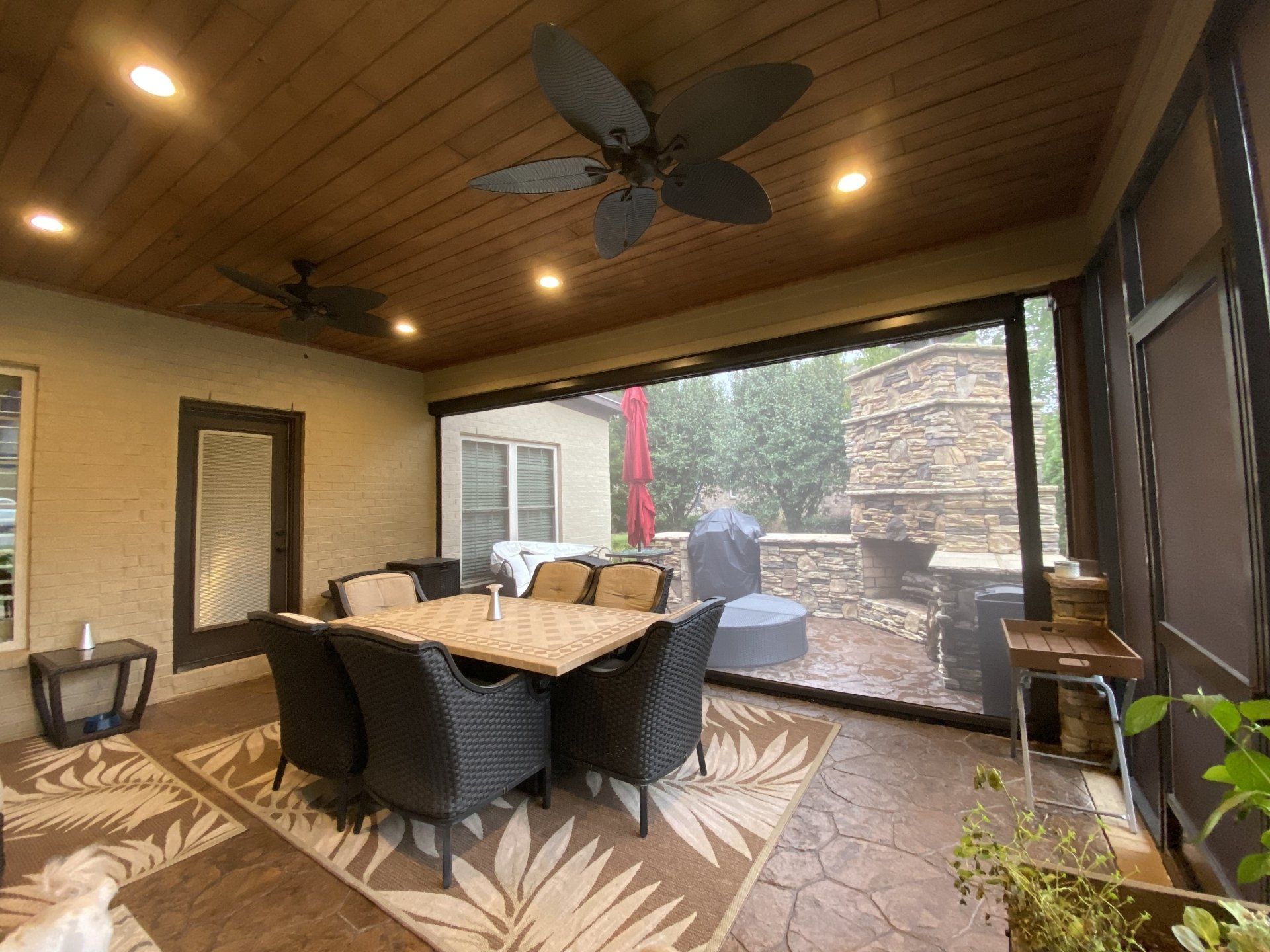 A screened in porch with a table and chairs and a ceiling fan.