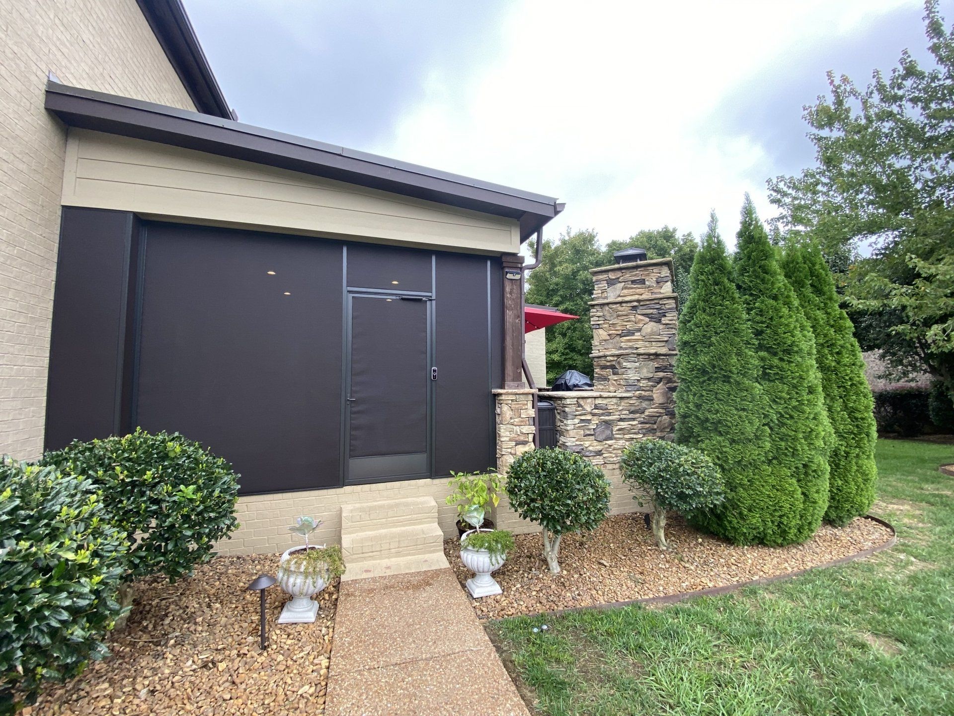 A house with a black garage door and a stone fireplace in the backyard.