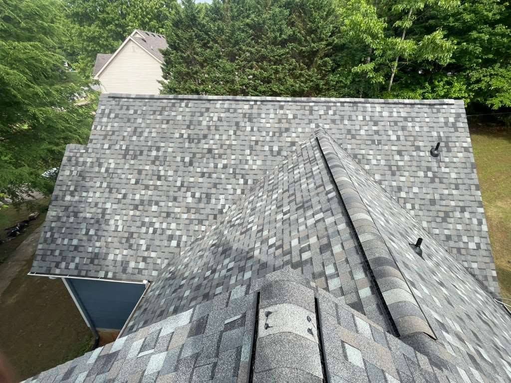 Gray shingled roof seen from above, with trees and a small building in the background