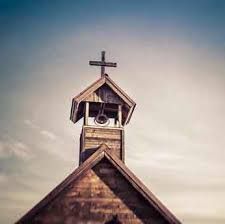 The wooden bell tower of a small church, topped with a cross, set against a soft, hazy sky.