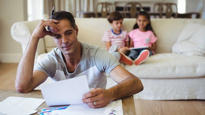 man looks distressed at a paper in his hand while 2 children sit in the background