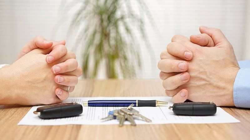 two people clasp sit across a table with keys and a pen on it