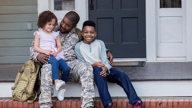 Man in military uniform hugs two children
