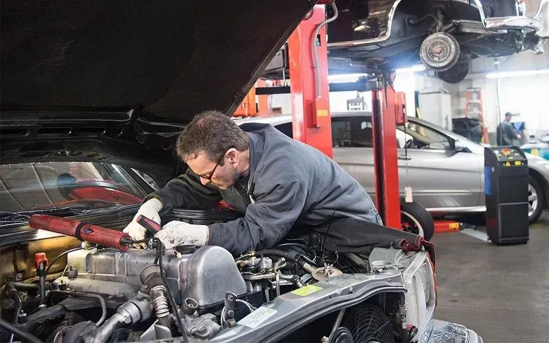 Mechanic working on car engine in repair shop.