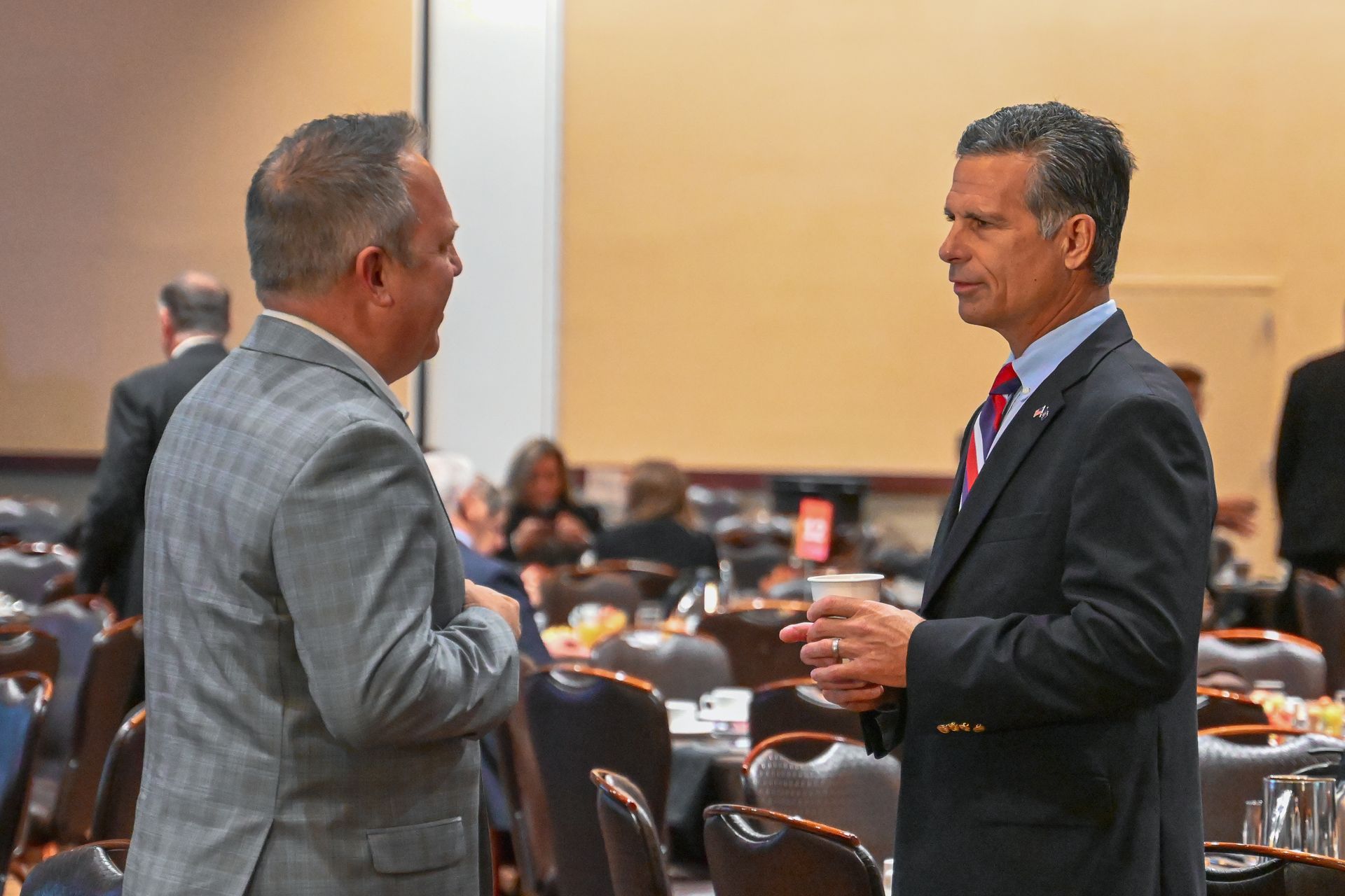 Two men in suits are talking to each other in a conference room.