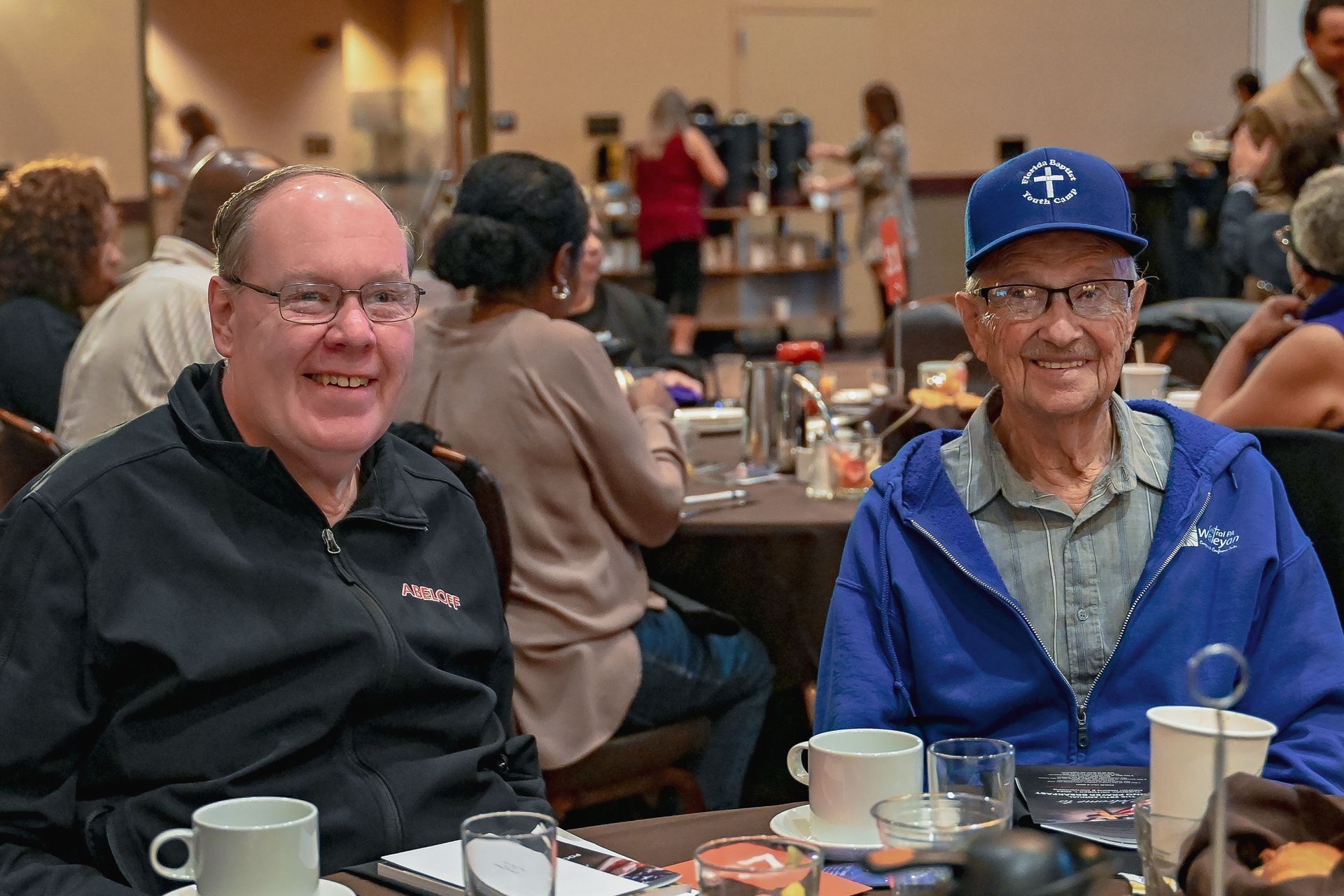 Two men are sitting at a table with cups of coffee.