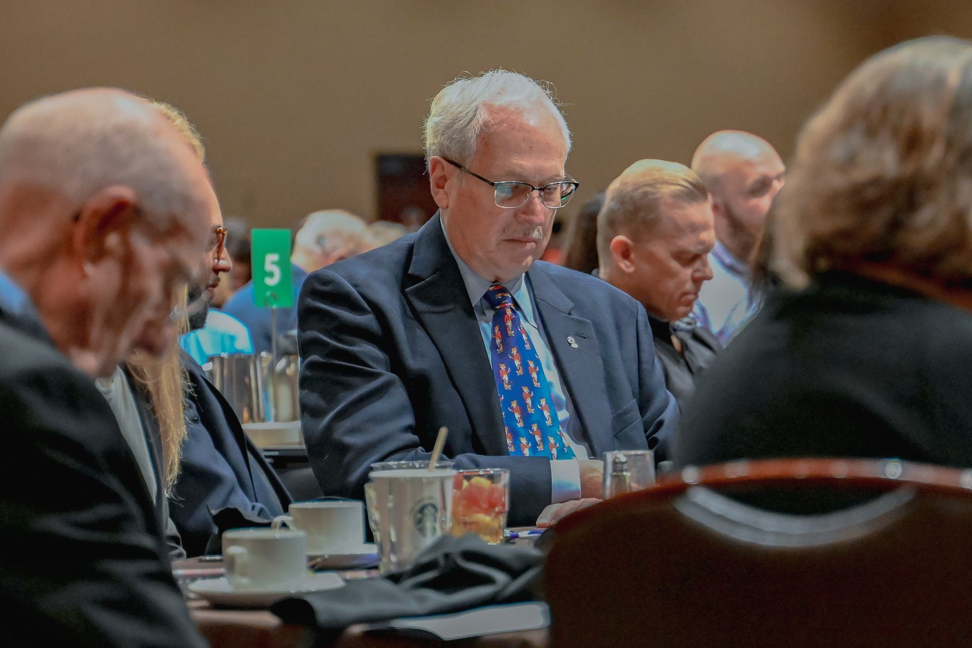 A man in a suit and tie is sitting at a table with other people.