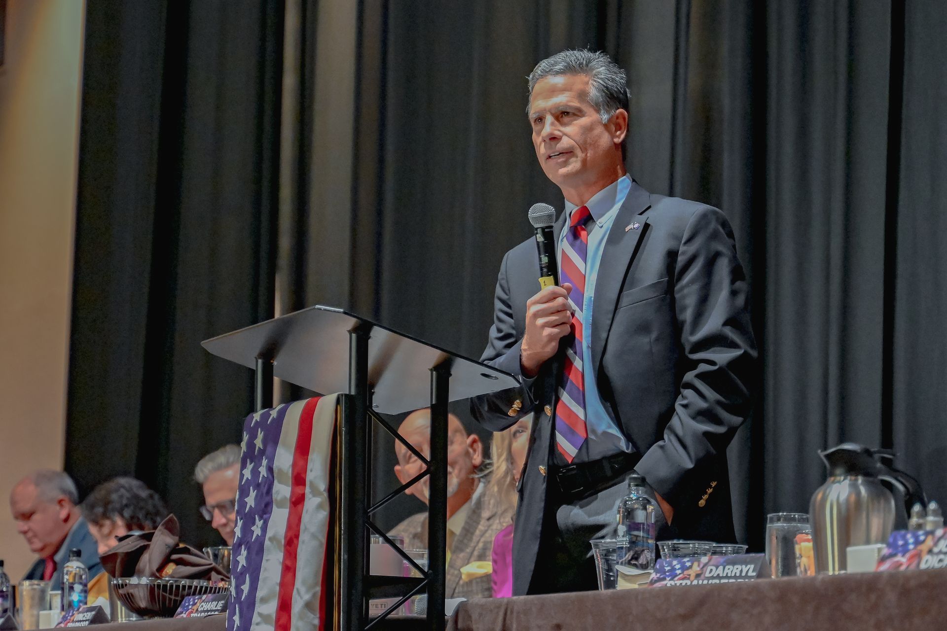 A man in a suit and tie is standing at a podium holding a microphone.