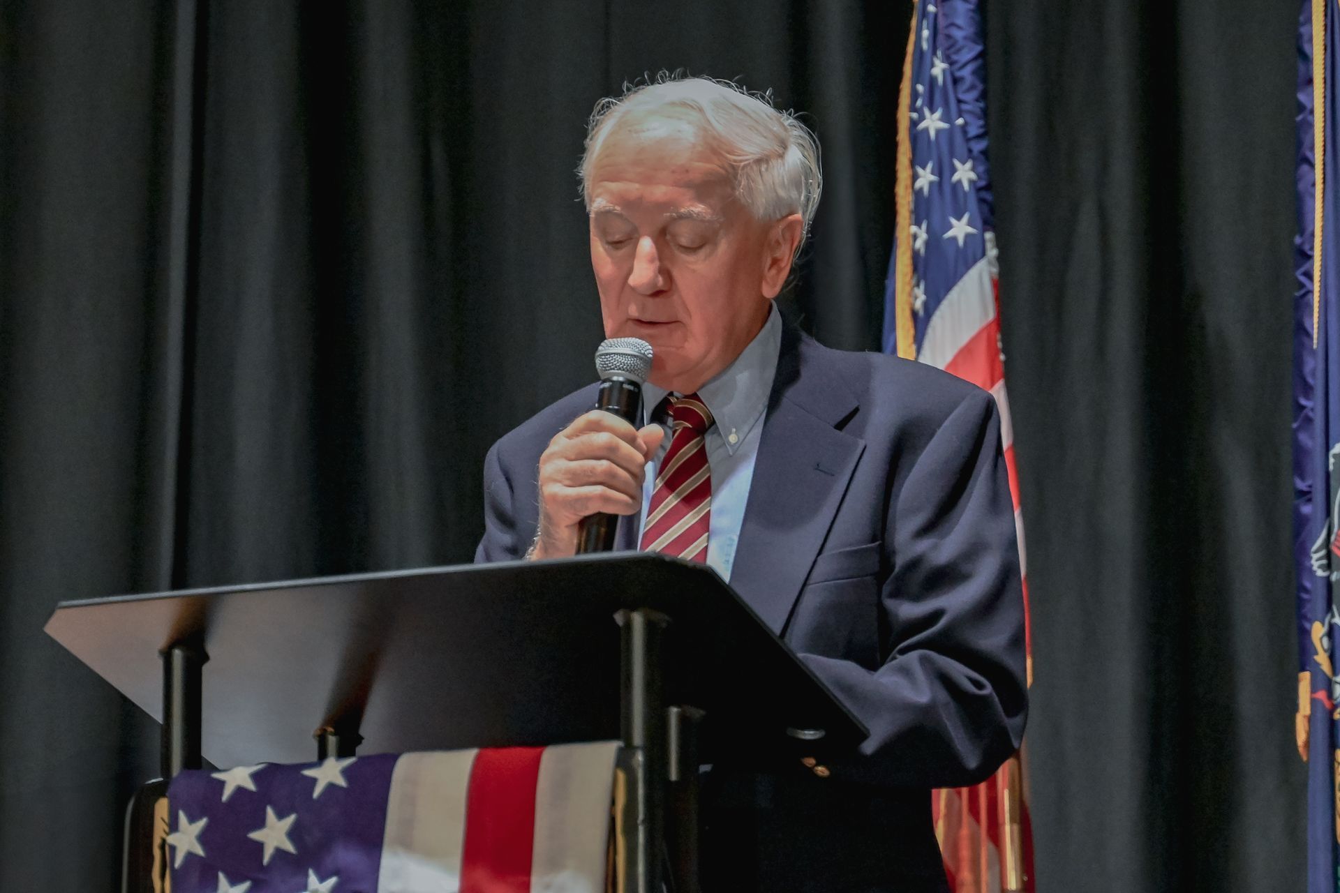 A man in a suit and tie is standing at a podium holding a microphone.