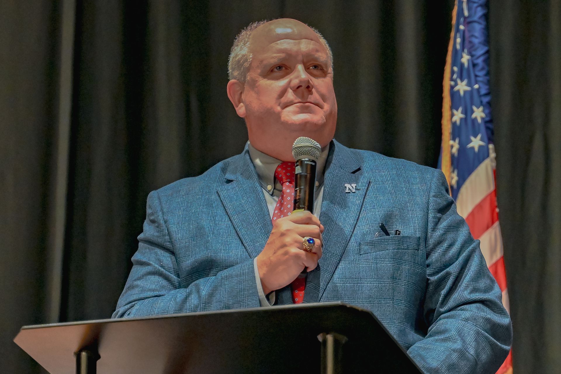 A man in a suit and tie is standing at a podium holding a microphone.
