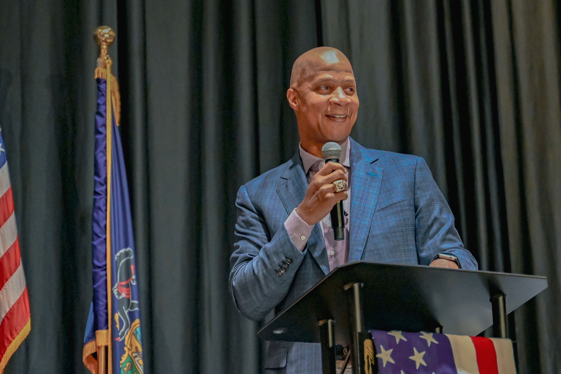 A man in a suit is standing at a podium holding a microphone.