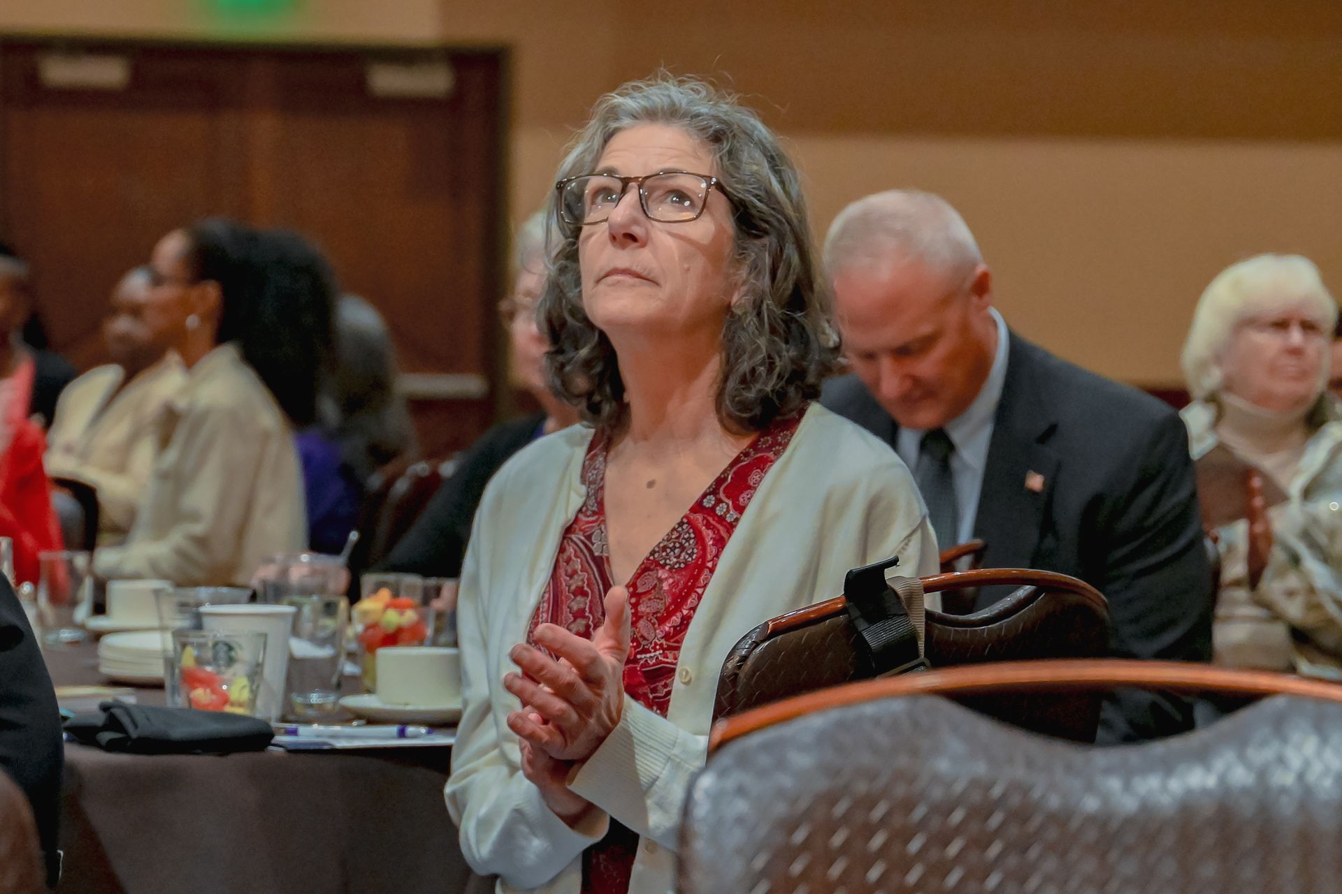A woman wearing glasses is clapping her hands while sitting at a table.
