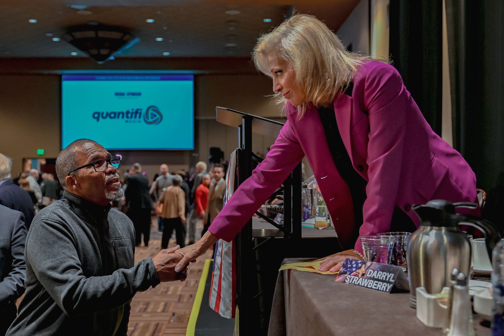 A woman in a pink jacket is shaking a man 's hand at a conference.