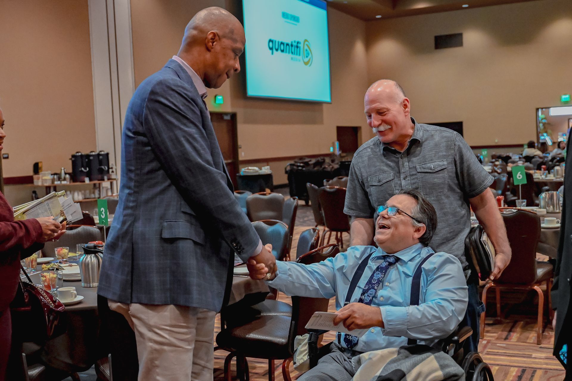 A man in a wheelchair is shaking hands with a man in a suit.