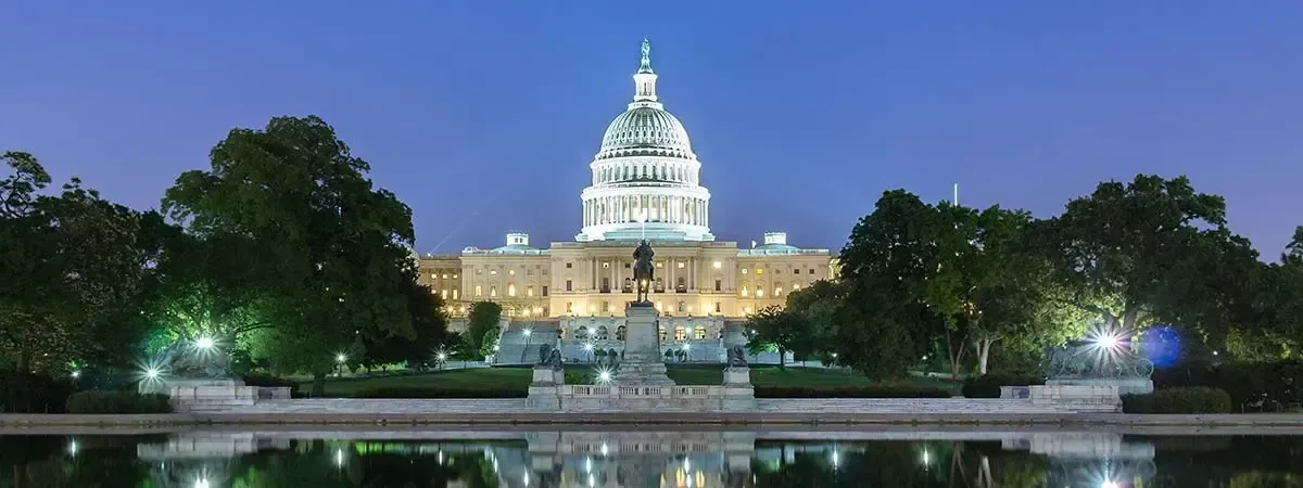 The capitol building is lit up at night and reflected in the water.