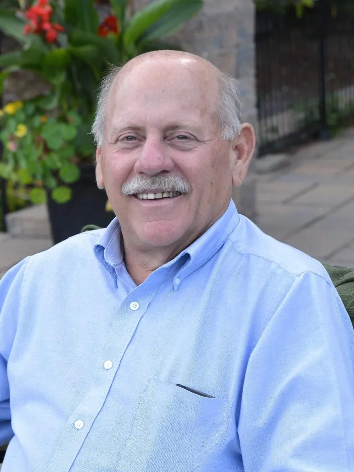 A man with a mustache is wearing a blue shirt and smiling.