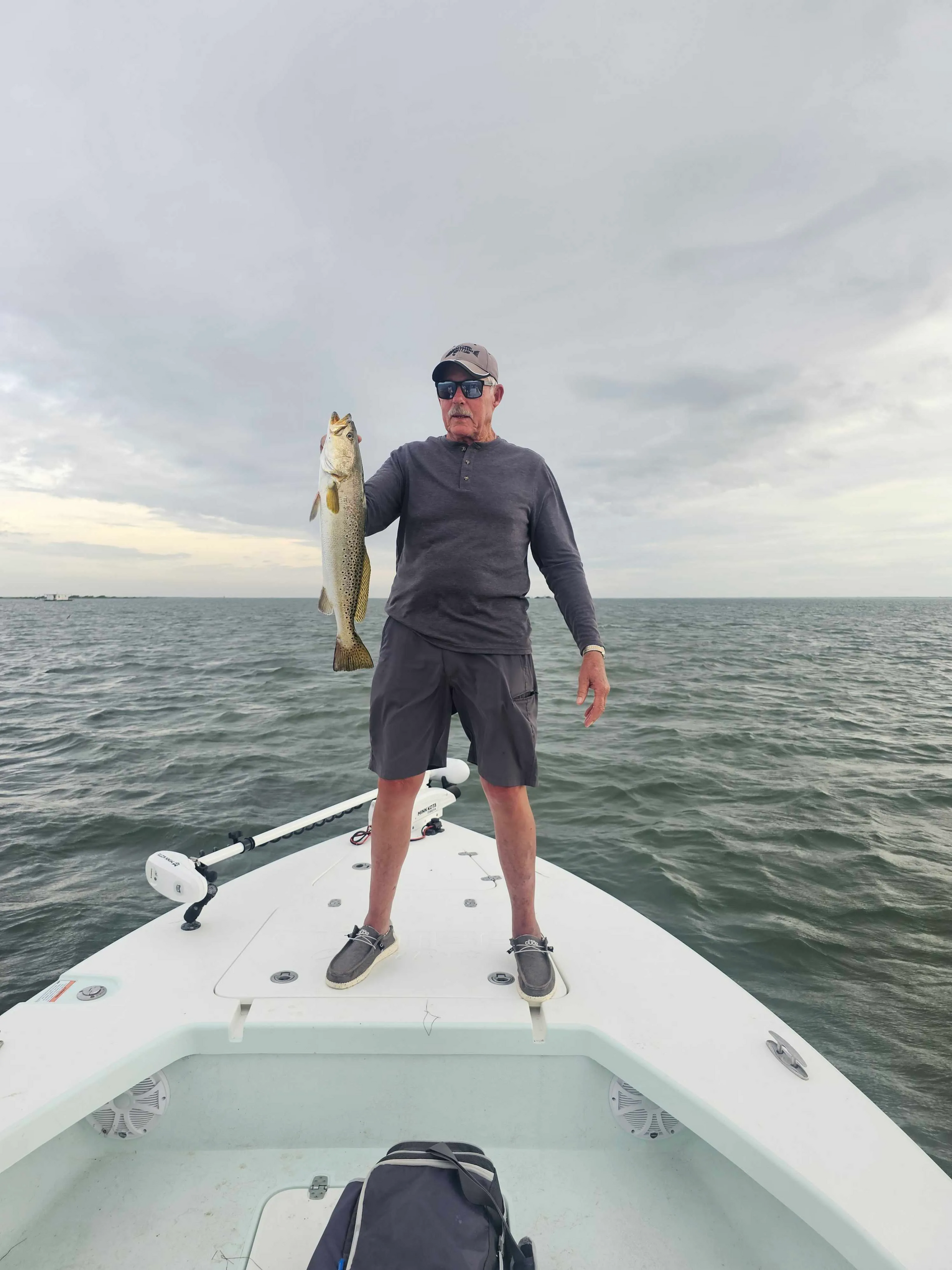 A man is standing on the back of a boat holding a fish.