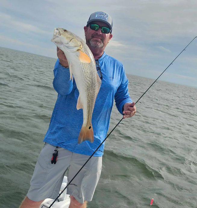 A man on a boat holding a fish and a fishing rod