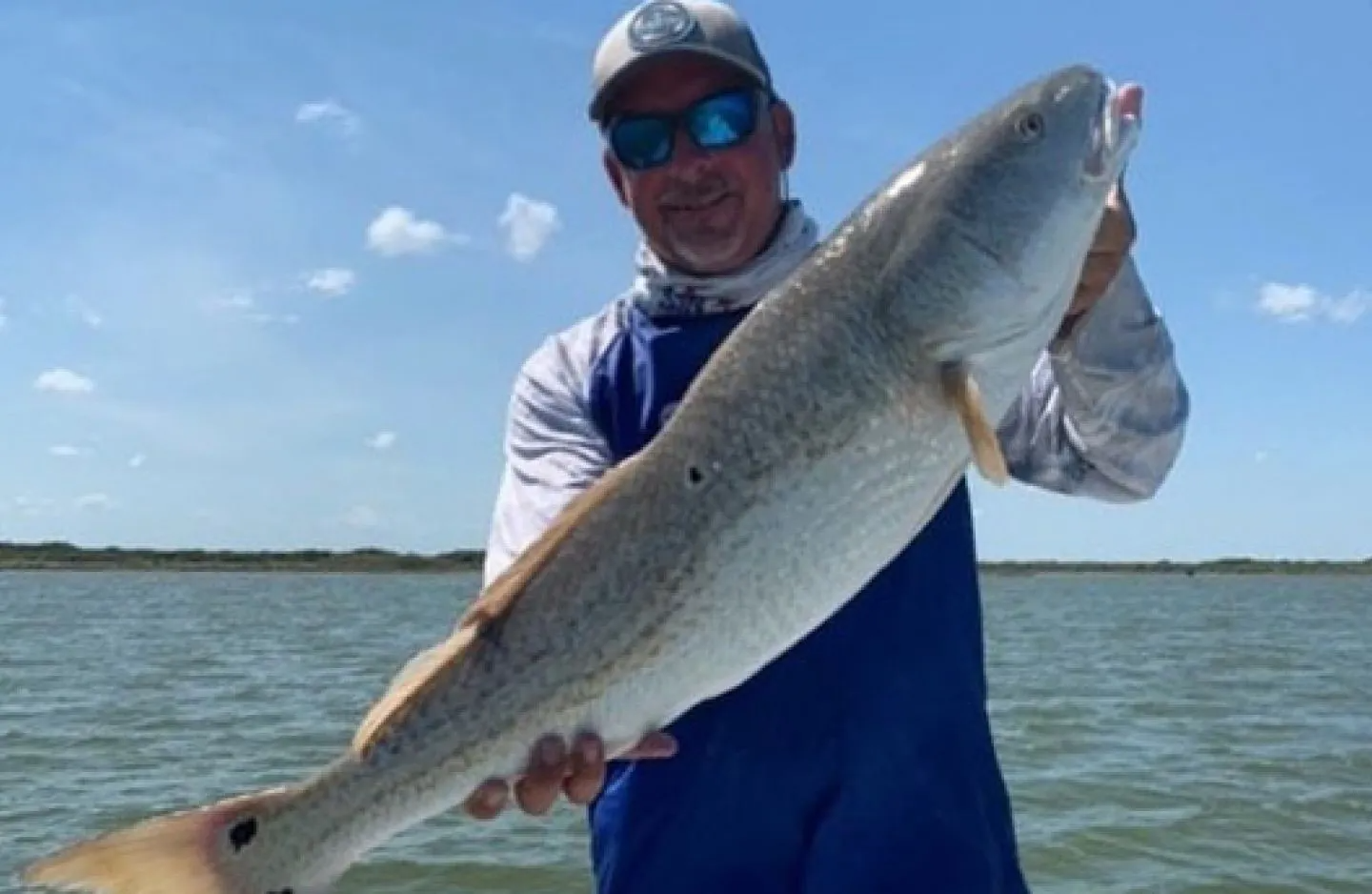 A man is holding a large fish in front of a body of water.