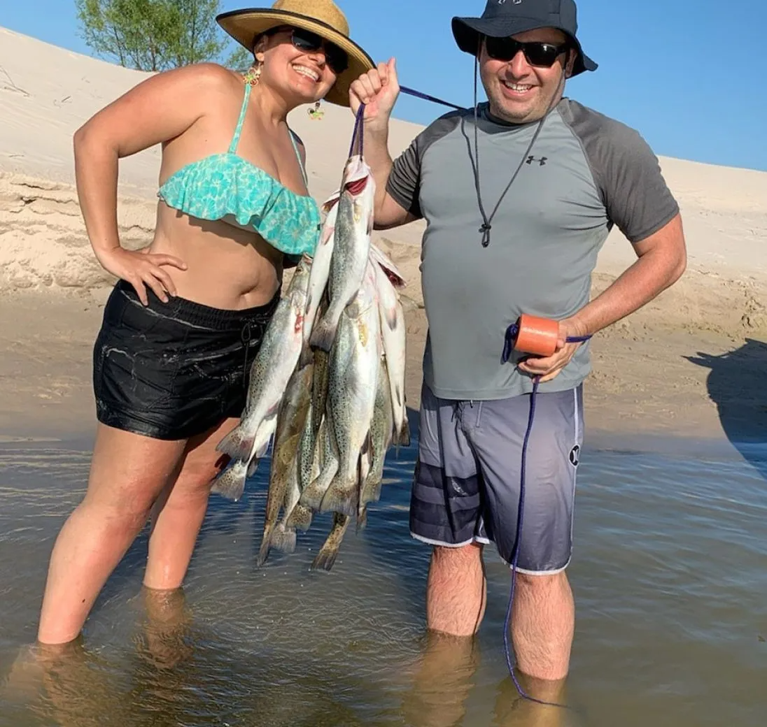 A man and a woman are standing in the water holding fish