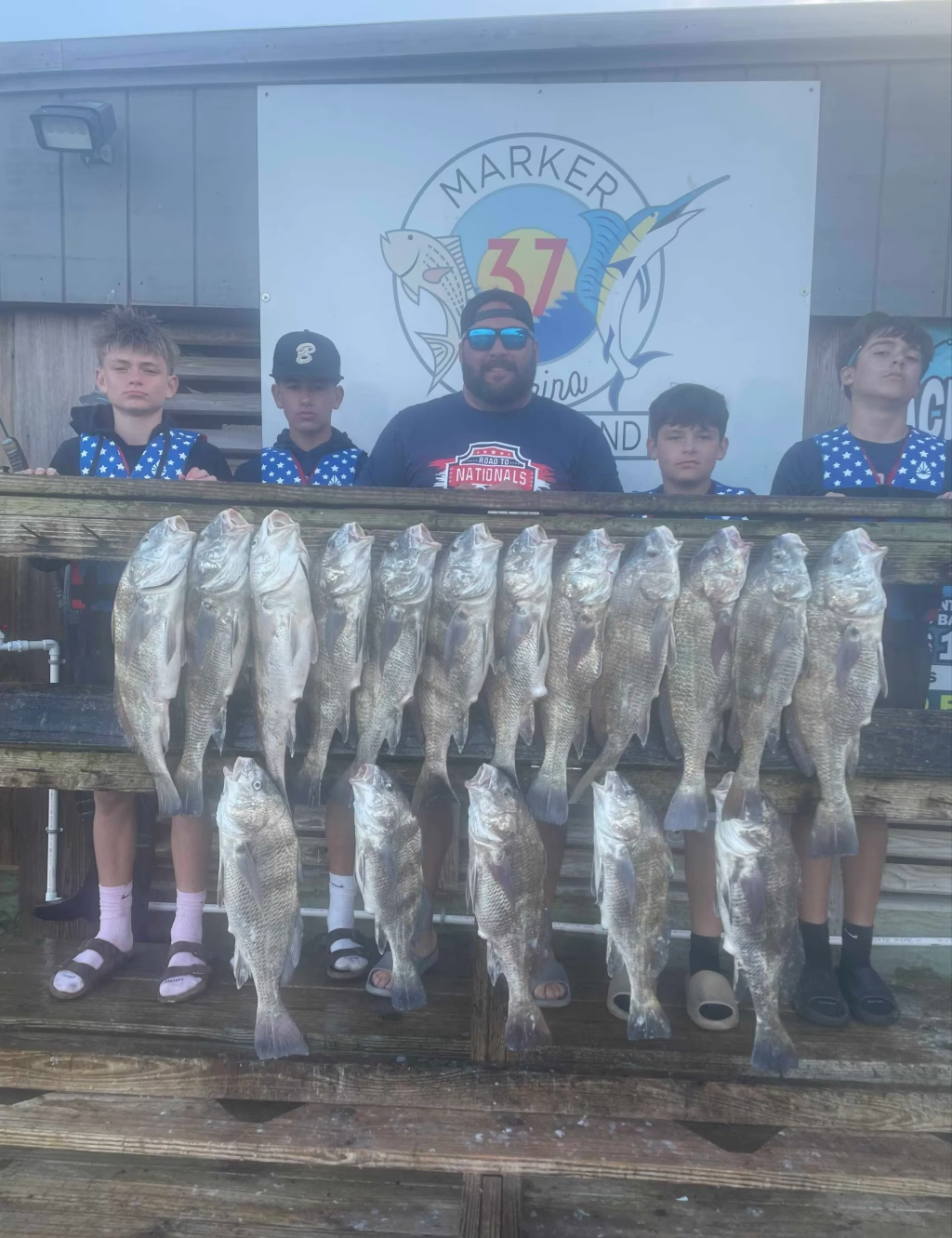 A group of young boys are standing next to a man holding a bunch of fish.