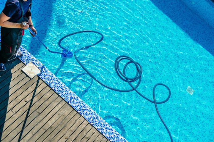 Pool cleaner hose floating in blue swimming pool beside a wooden deck