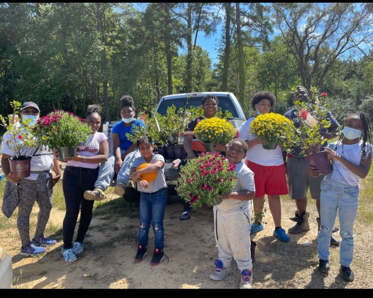 A group of people are holding potted plants in front of a truck.