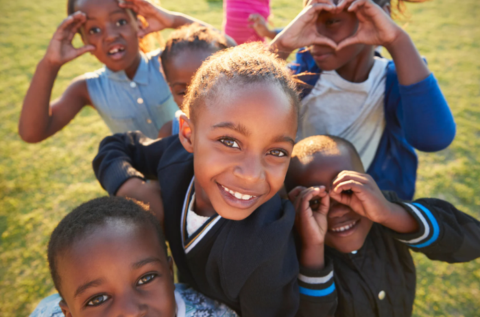 A group of children are making a heart shape with their hands.