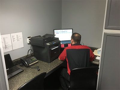 A person in a red shirt works at a desk with a computer and printer in a small office. |  Johnson's Automotive