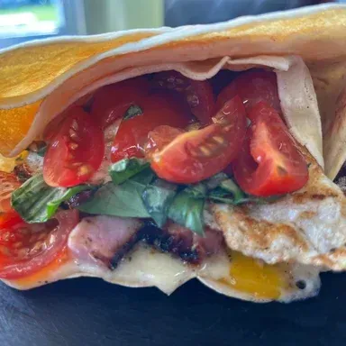 Close-up of a toasted sandwich with tomato, greens, melted cheese, and grilled filling.