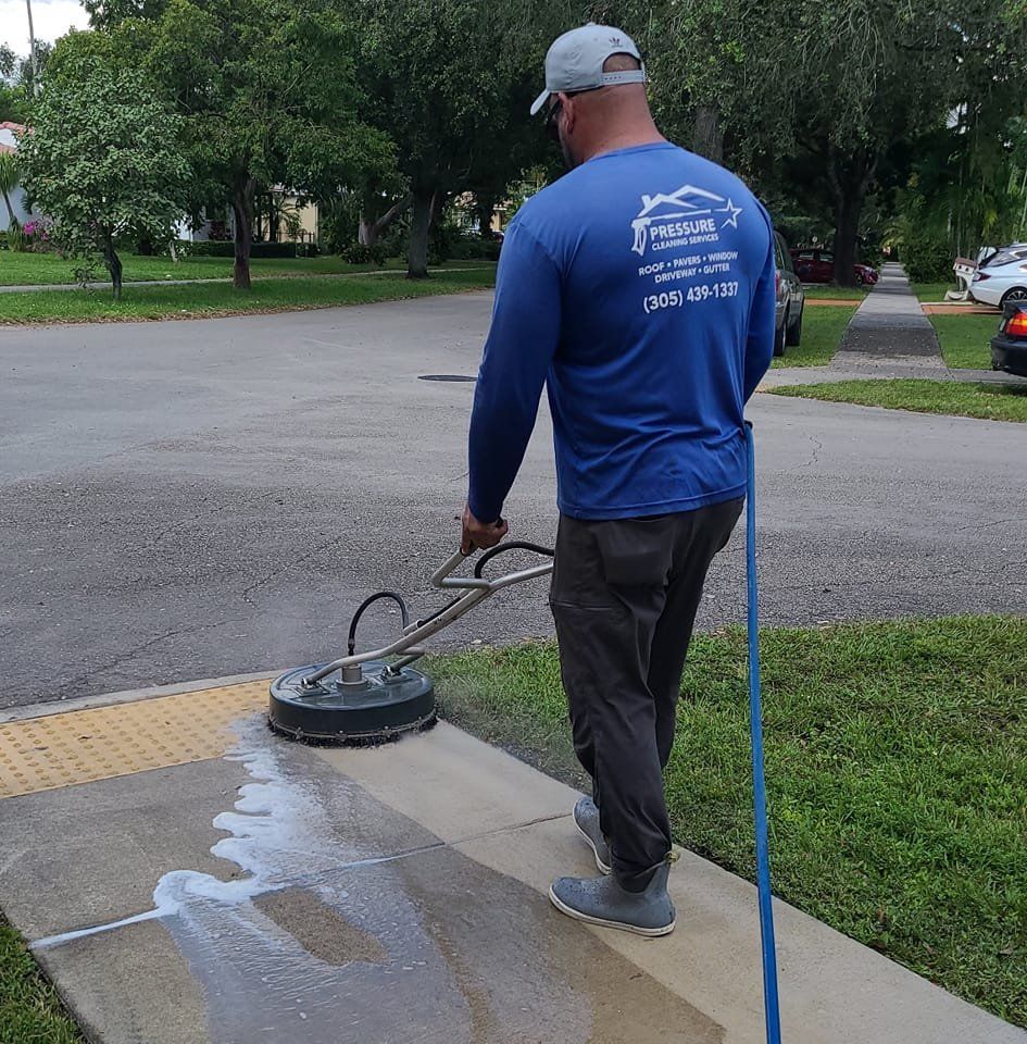 A man in a blue shirt is cleaning a sidewalk with a machine